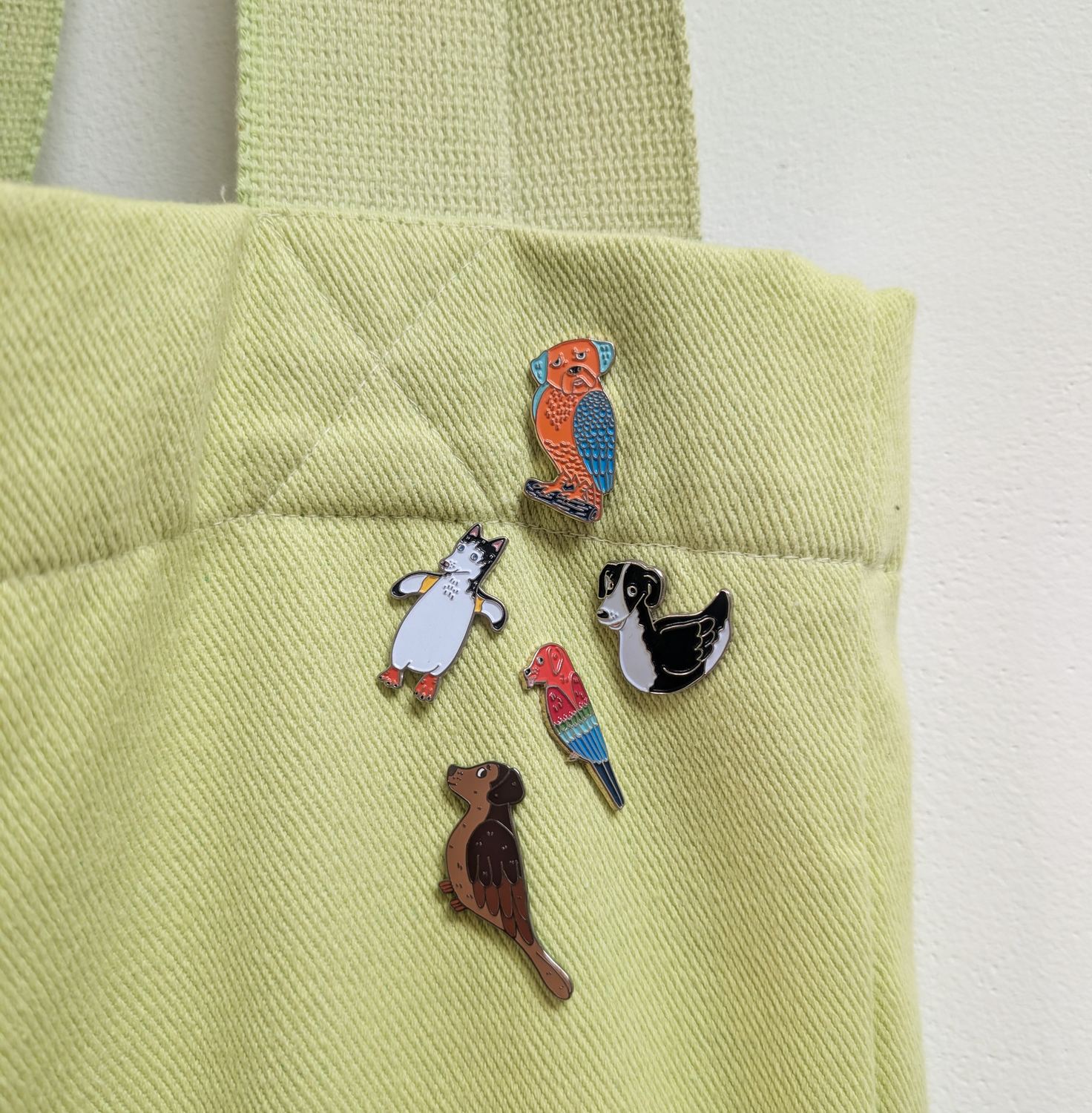Five dird pins — dogs' heads on birds' bodies — arranged on the front of a lime green tote bag