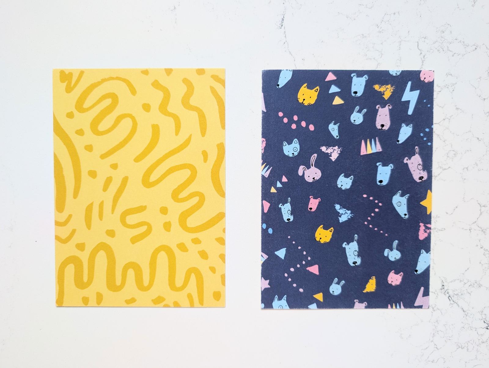 Two postcards: yellow squiggles on yellow, and a navy card scattered with small pastel dog faces